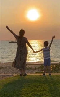 Two people with hands up in front of sunset at the beach